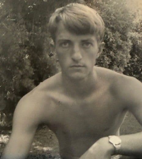 A faded sepia photograph of a young man sitting outdoors, the colour washed out by decades in an album