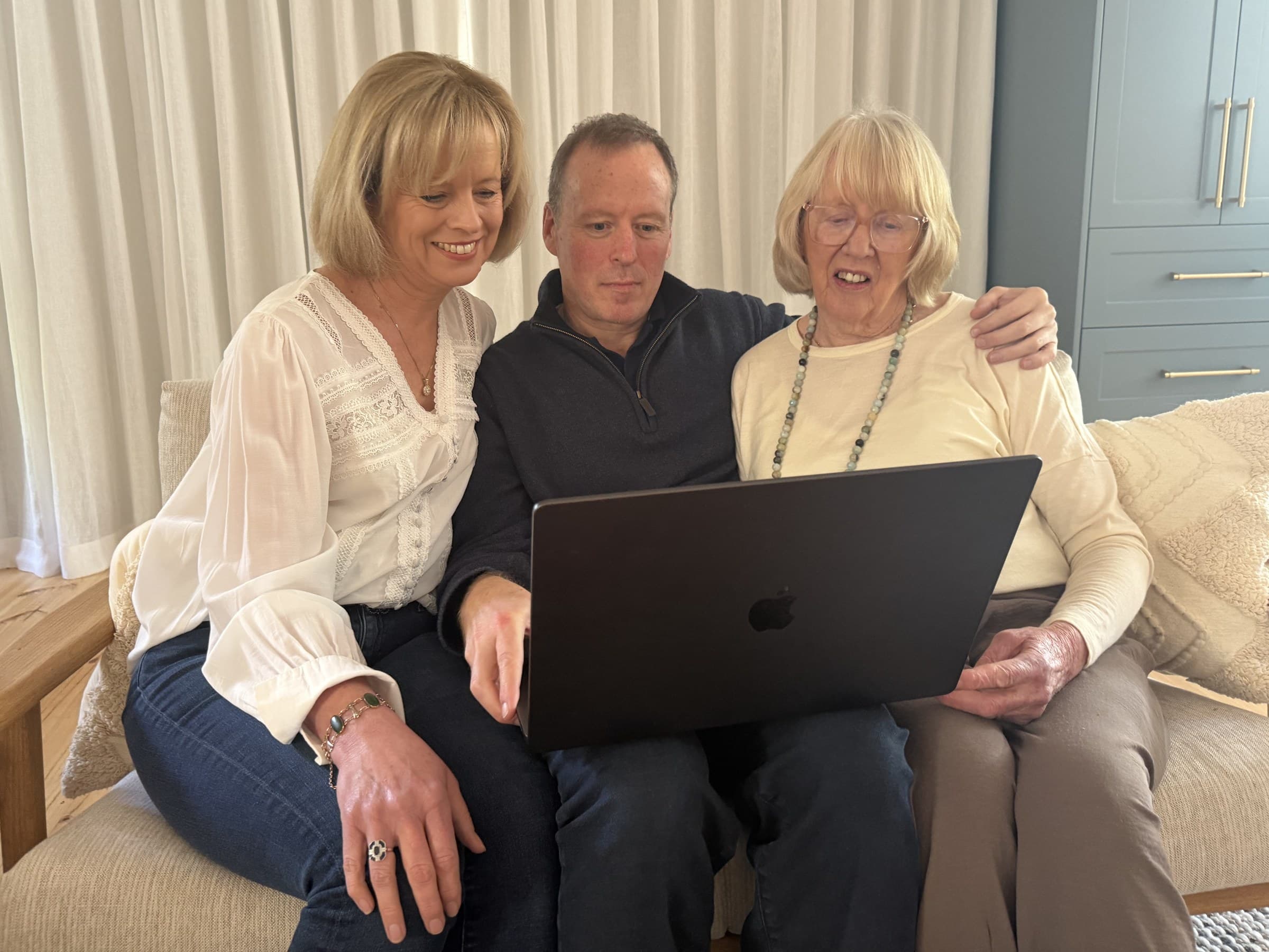 Three family members looking at a laptop together on a sofa