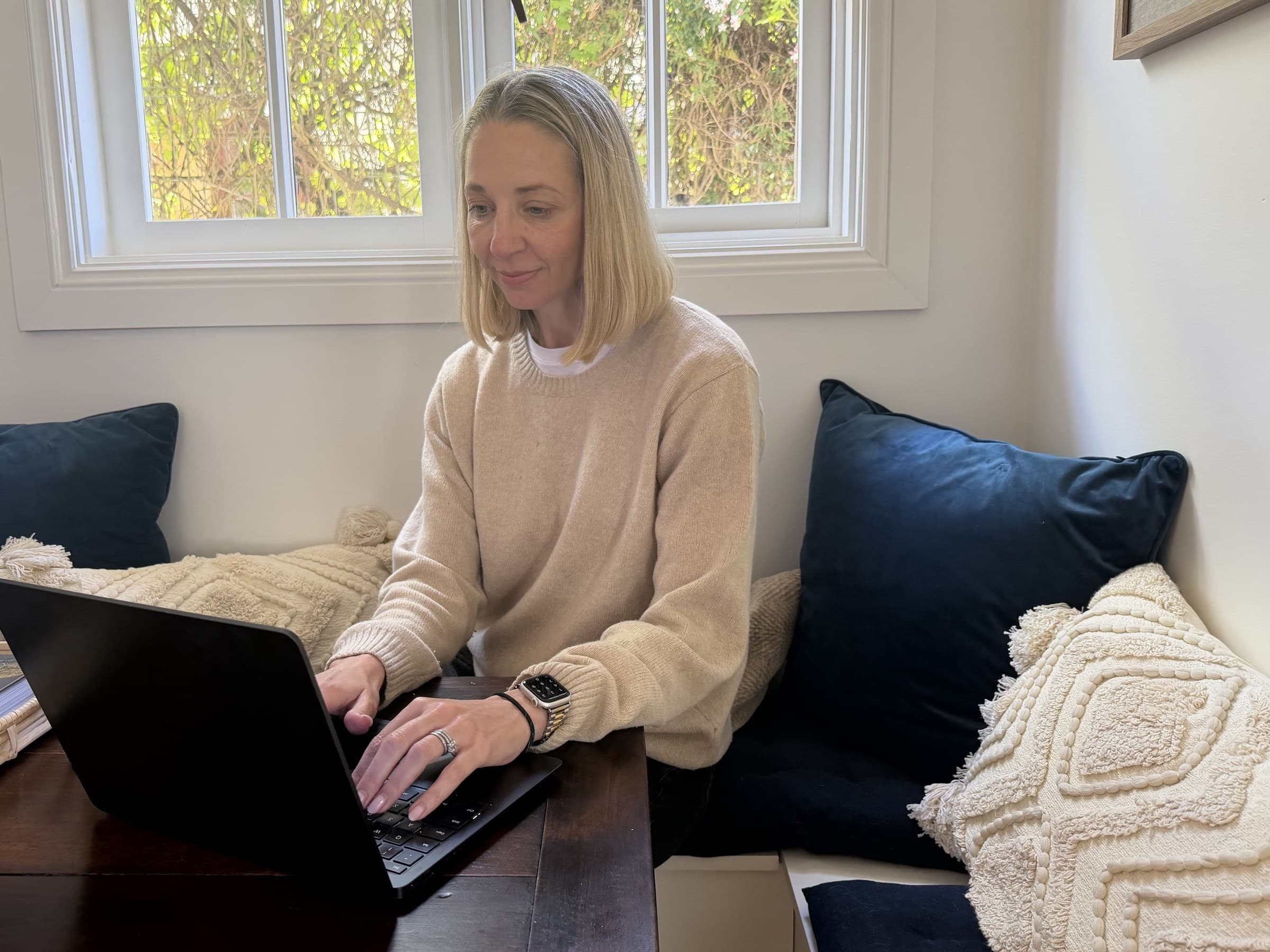 A woman typing on a laptop at a window seat